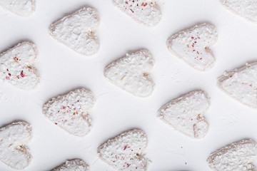  A pattern of Valentine's day white coconut heart shaped cookies on a white background  with red sprinkles. Copy space. Monochrome