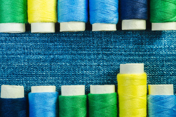 Spools of blue, yellow and green  sewing thread arranged in two rows on denim with copy space