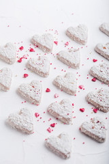  A pattern of Valentine's day white coconut heart shaped cookies on a white background  with red sprinkles. Copy space. Monochrome