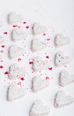  A pattern of Valentine's day white coconut heart shaped cookies on a white background  with red sprinkles. Copy space. Monochrome