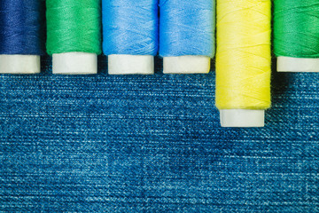 Spools of blue, yellow and green  sewing thread arranged in row on denim with copy space