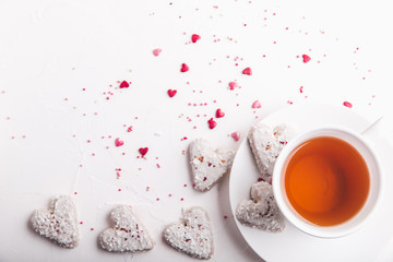 Obraz na płótnie Canvas White tea cup with tea and Valentine's day white coconut heart shaped cookies with red and pink heart sprinkles. Copy space