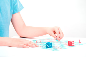 Child plays a board game snakes and ladders with colorful pieces and dice with both hands on tabletop. Copy space