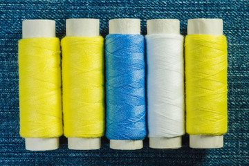 Spools of white, yellow and green  sewing thread arranged in row on denim