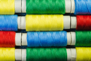 Spools of blue, yellow, red and green  sewing thread arranged in rows on denim