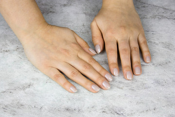 close up of beautiful female hands with manicure on marble table,  healthy hands skin and nails concept