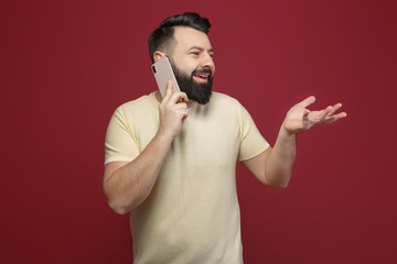 A cute and bearded brunette man on a red background says emotionally on the phone