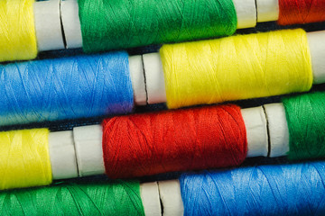 Spools of blue, yellow, red and green  sewing thread arranged in rows on denim