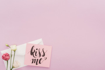 top view of flowers, envelope and card with 'kiss me' lettering isolated on pink