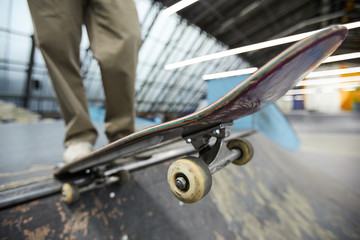Skateboard above edge of descent held by leg of young parkour guy during training on stadium
