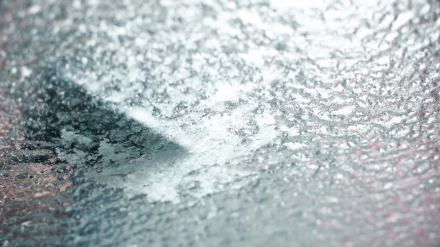 Color footage of a person scraping the ice on a car's windshield.