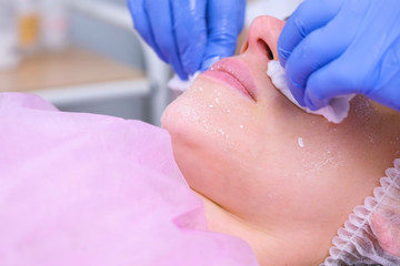 Beautician washes woman's face using cotton pads from mask. Cleaning face. Lips and chin close-up.