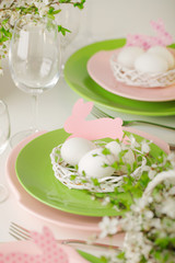 Happy easter. Decor and table setting of the Easter table - Branches of flowering spring tree, dishes of pink and green color.