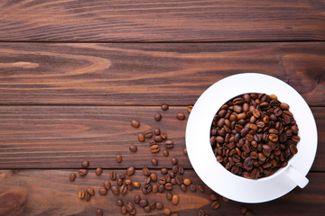 Coffee beans in cup on brown wooden background.
