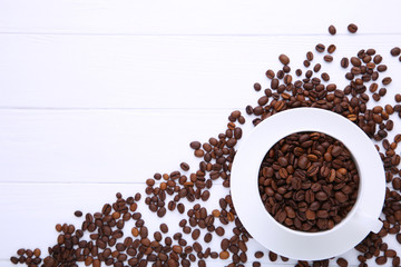 Coffee beans in cup on white wooden background.