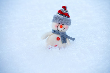 Happy funny snowman in the snow. The snowman is wearing a fur hat and scarf. The concept of winter, cold, holiday.