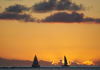 Sunset at the beach in Black River, Mauritius with sailing boats on the horizon with a beathtaking orange sky and clouds.