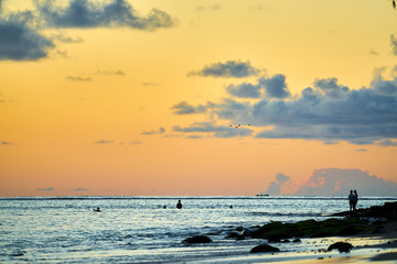 Naklejka na ściany i meble Swimming at sunset in Black River, Mauritius with rocks, beach and a romanitc couple gasing over the ocean.