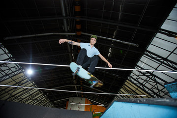 Agile guy in casualwear standing on board while flying over parkour area edge during training