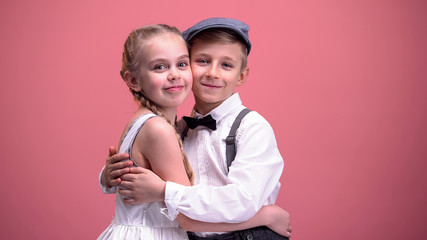 Happy kids couple hugging and looking to camera, isolated on pink background