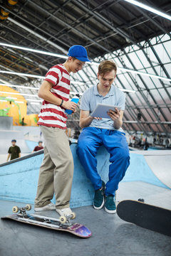 Two casual guys with tablet watching curious video about parkour stunts after training at stadium