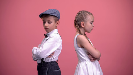 Little male looking at offended young girlfriend, standing back to each other