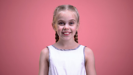 Pretty little female happily looking into camera, isolated on pink background