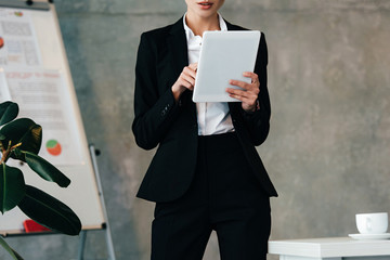 Cropped view of young businesswoman staying by work desk and using digital tablet