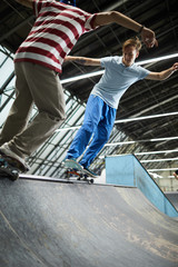 Two active casual boys on skateboards sliding down off edge of parkour facilities during training at leisure