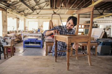 Furniture maker sanding a chair on workshop bench - obrazy, fototapety, plakaty