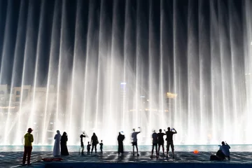 Poster Silhouettes of people enjoying the fountain show in Dubai at night, United Arab Emirates © Delphotostock