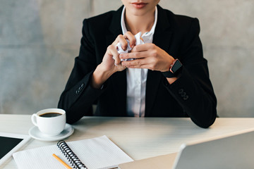 cropped view of businesswoman sitting at workplace with crumpled paper in hands