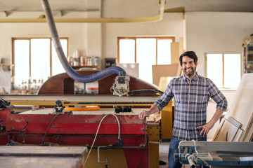 Fototapeta na wymiar Smiling woodworker standing by equipment in his workshop