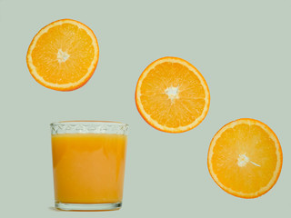 Glass with fresh orange juice, flying orange slices on a white, isolated background. Close-up. Concept of tasty and healthy food