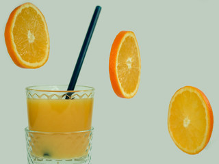 Glass with fresh orange juice, flying orange slices on a white, isolated background. Close-up. Concept of tasty and healthy food