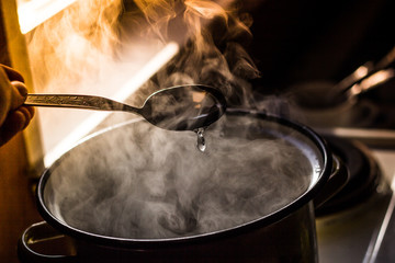 the man stirs the soup in the pan from which steam comes