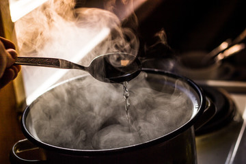 the man stirs the soup in the pan from which steam comes