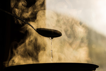 the man stirs the soup in the pan from which steam comes