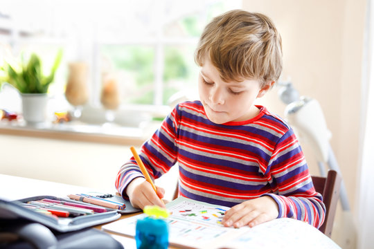 Happy smiling little kid boy at home making homework at the morning before the school starts. Little child doing excercise, indoors. Elementary school and education: Boy drawing geometric figures