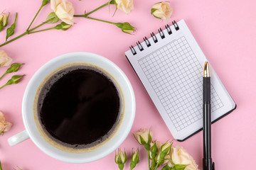 Beautiful mini roses with a cup of coffee and a notebook on a bright pink background. holidays. Valentine's Day. women's Day. top view.
