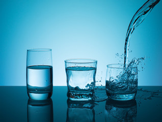 Creative splashing water in the glass on blue background.