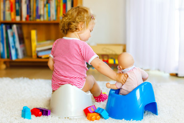 Closeup of cute little 12 months old toddler baby girl child sitting on potty. Kid playing with...