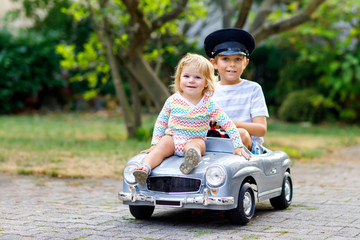 Two happy children playing with big old toy car in summer garden, outdoors. Kid boy driving car...