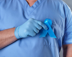 doctor in uniform and latex gloves holding a blue ribbon in his hand