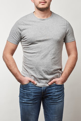 partial view of man with hands in pockets in t-shirt with copy space isolated on grey