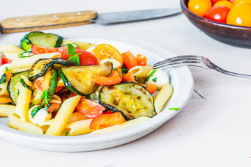 Margarita pasta in a plate on a wooden table - penne with tomatoes, zucchini, mozzarella and basil