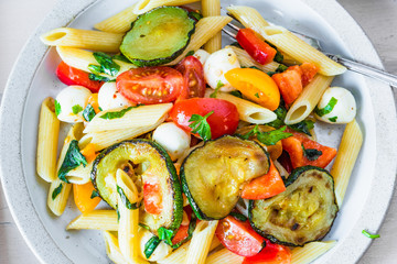 Closeup margarita pasta, warm penne salad with tomatoes, zucchini, mozzarella and basil.