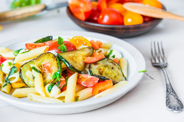 Margarita pasta on a plate and cherry tomatoes in the background - penne with tomatoes, zucchini, mozzarella and basil.