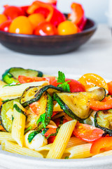 Margarita pasta on a plate and cherry tomatoes in the background - penne with tomatoes, zucchini, mozzarella and basil.