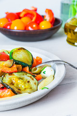 Margarita pasta on a plate and cherry tomatoes in the background - penne with tomatoes, zucchini, mozzarella and basil.